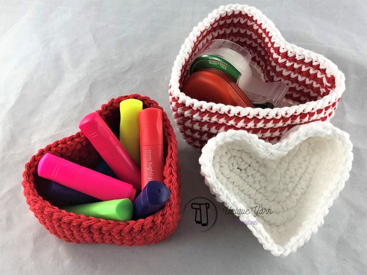 two crocheted baskets filled with markers, pens and pencils on top of a white sheet