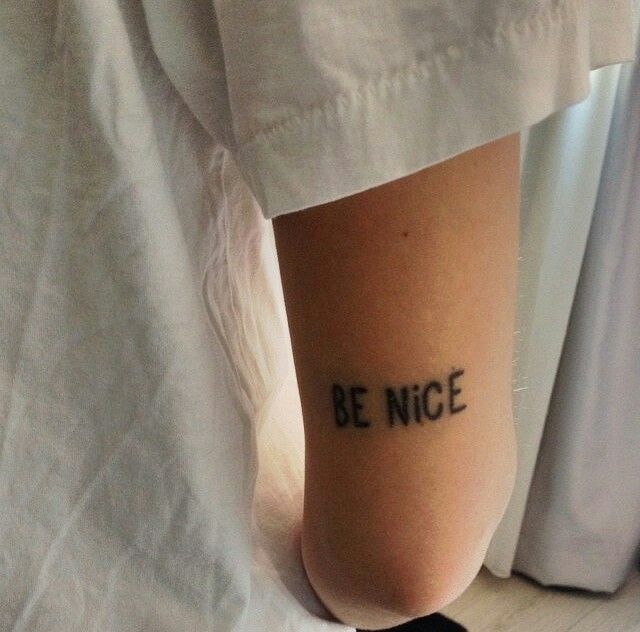 someone with a tattoo saying be nice on their leg