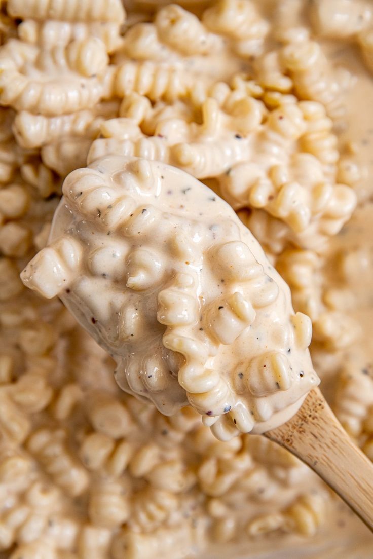 macaroni and cheese being stirred with a wooden spoon in a white sauce mixture