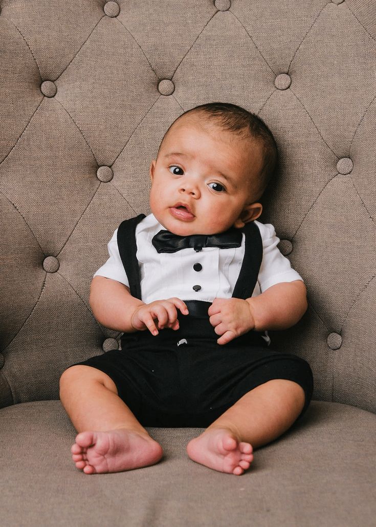 a baby sitting on top of a couch wearing a black bow tie and suspenders