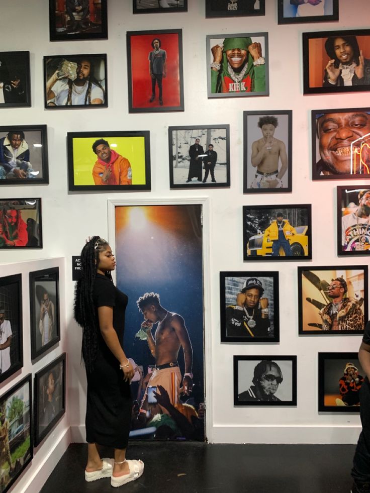 a woman standing next to a wall covered in pictures