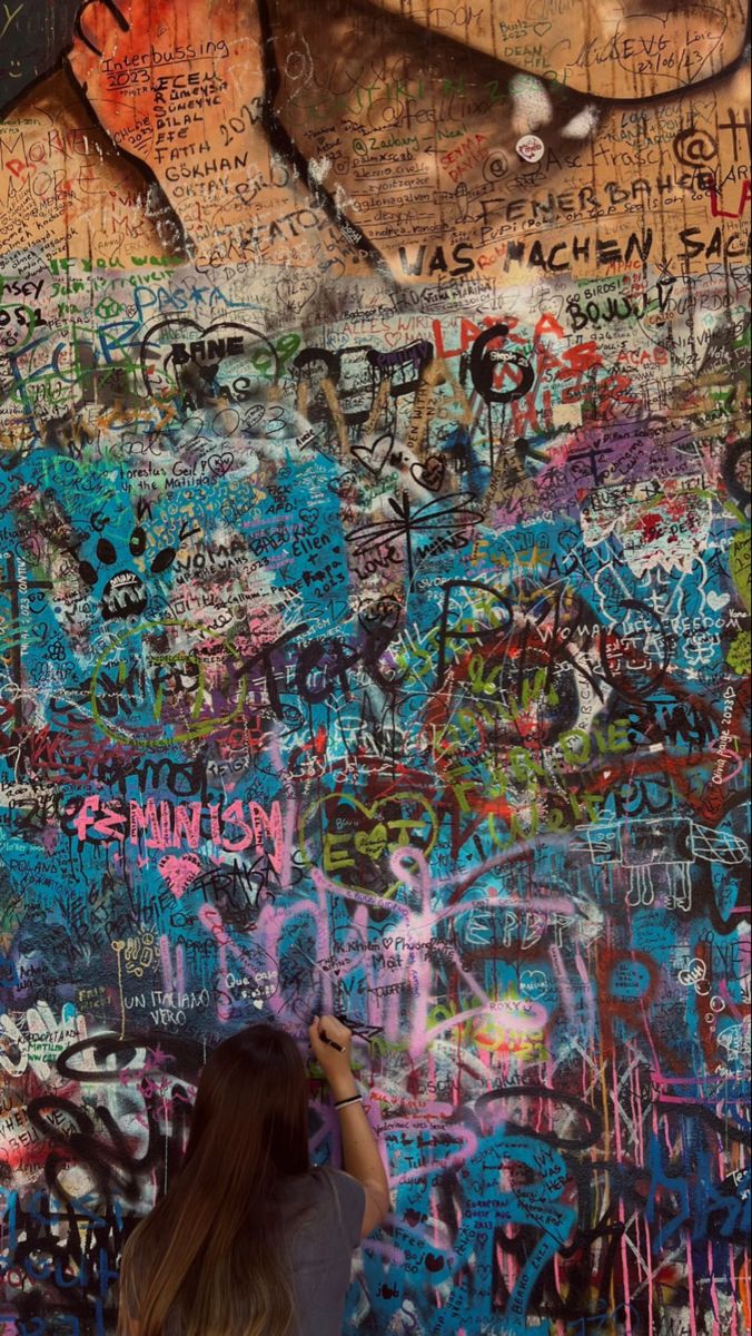 a woman writing on a wall covered in graffiti