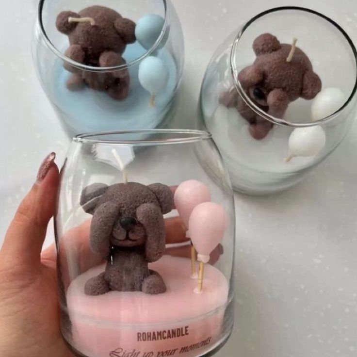 someone is holding a small teddy bear in a glass cup with candles inside it and some balloons on the side