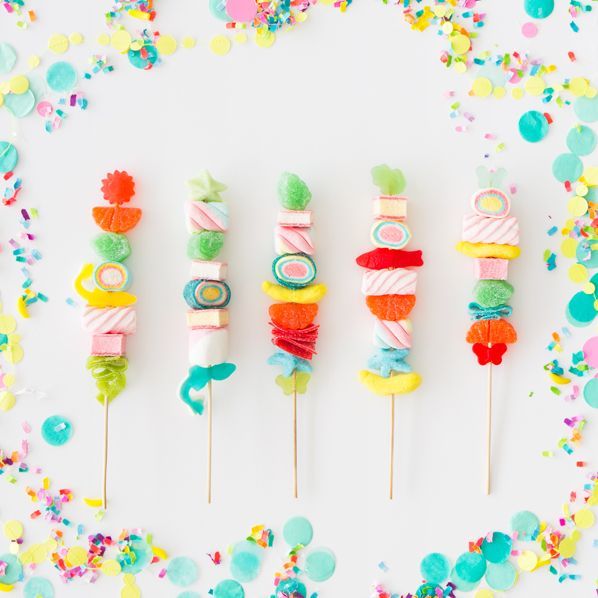 colorful candy lollipops are lined up on a white surface surrounded by confetti and sprinkles