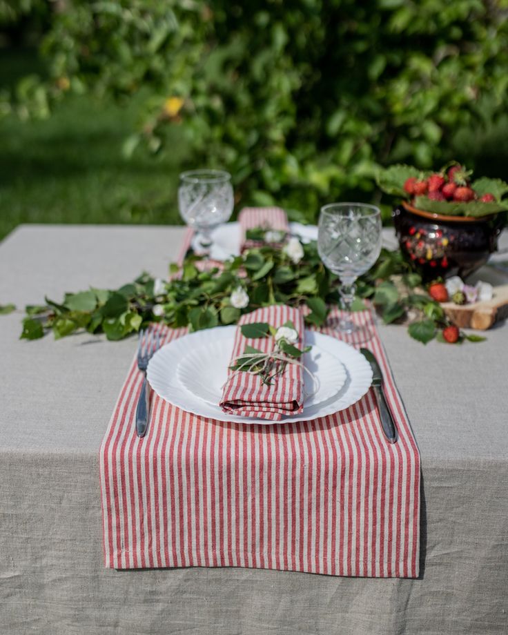 the table is set with red and white striped napkins, silverware, and strawberries