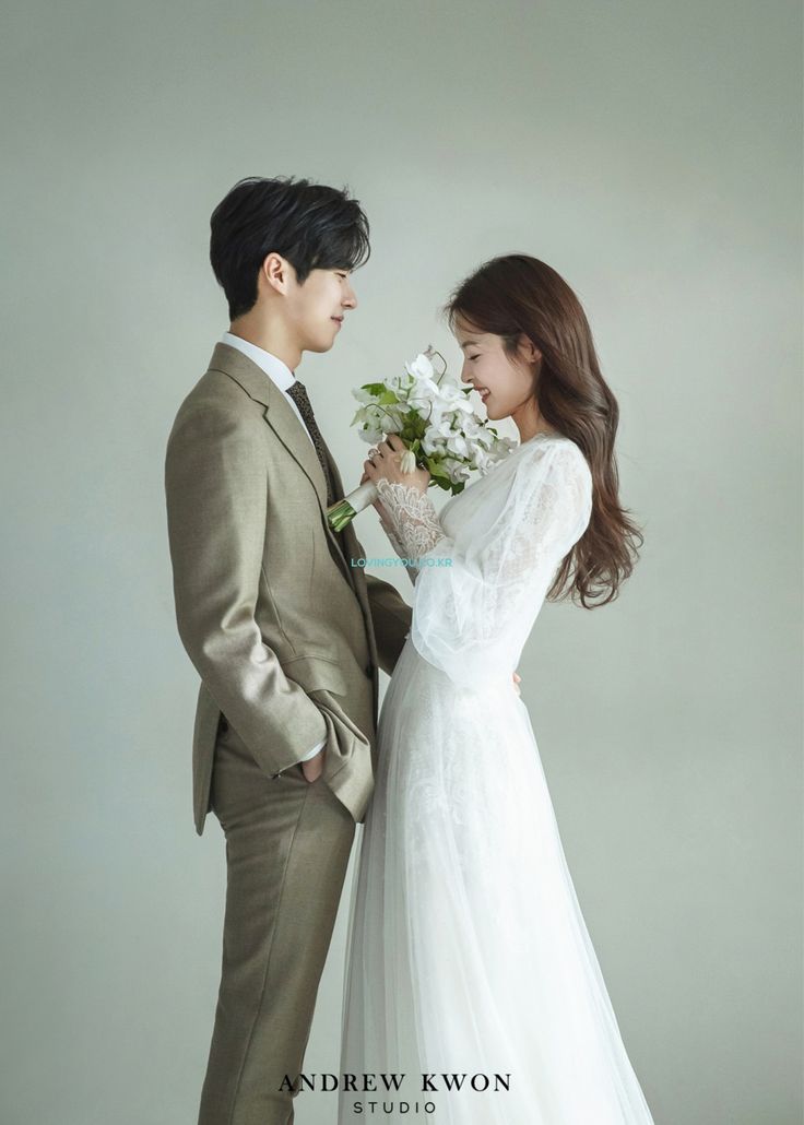 a man and woman standing next to each other in front of a white wall holding flowers