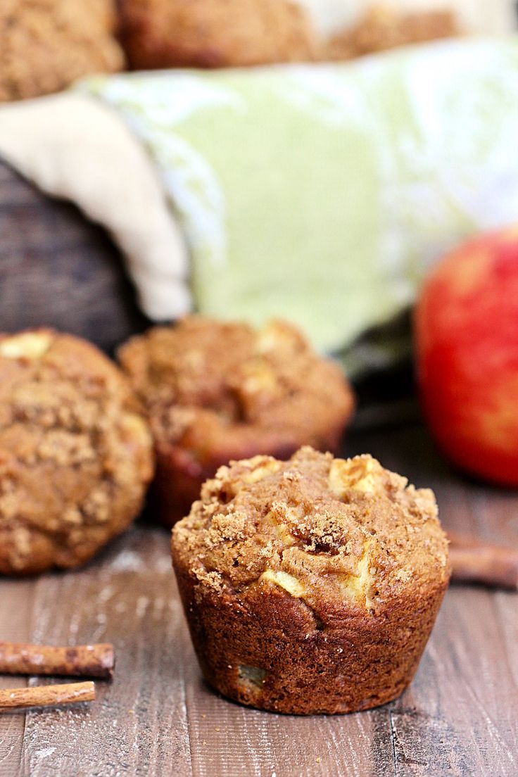 two muffins sitting on top of a wooden table next to an apple and cinnamon stick