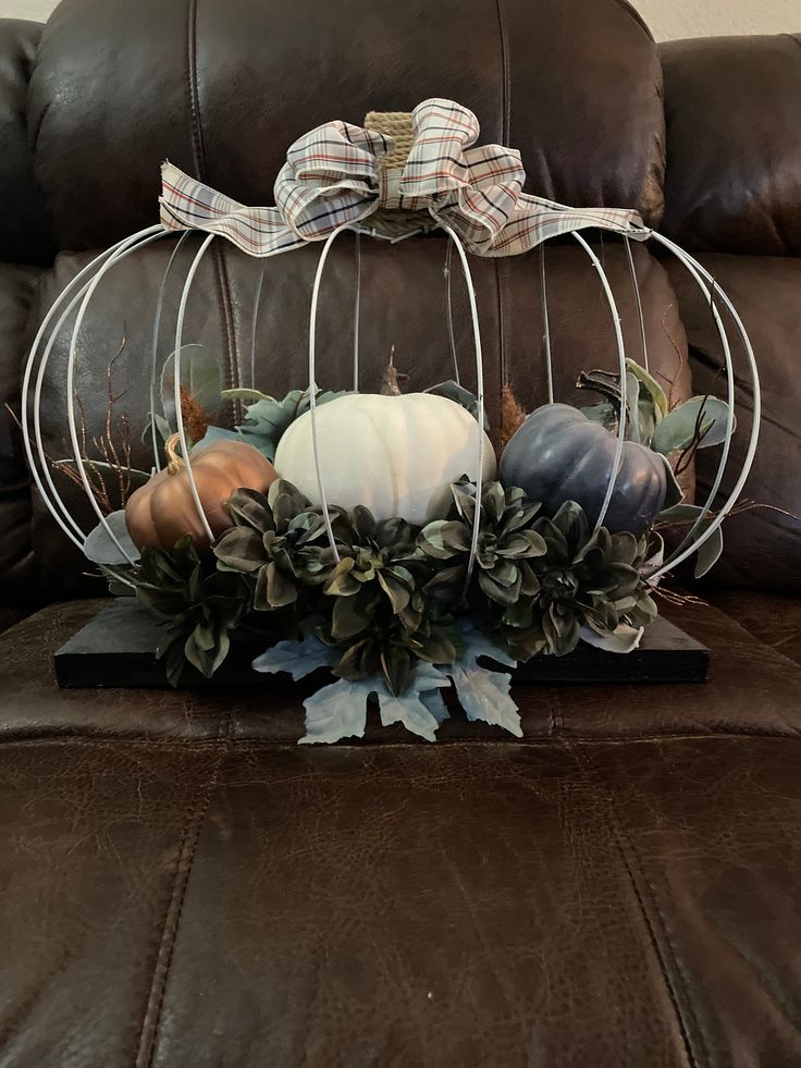 pumpkins and greenery sit in a wire basket on a leather couch with a plaid bow