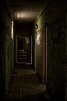 a dark hallway with graffiti all over the walls and floor, leading to another room