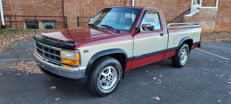 a red and white pickup truck parked in a parking lot next to a brick building