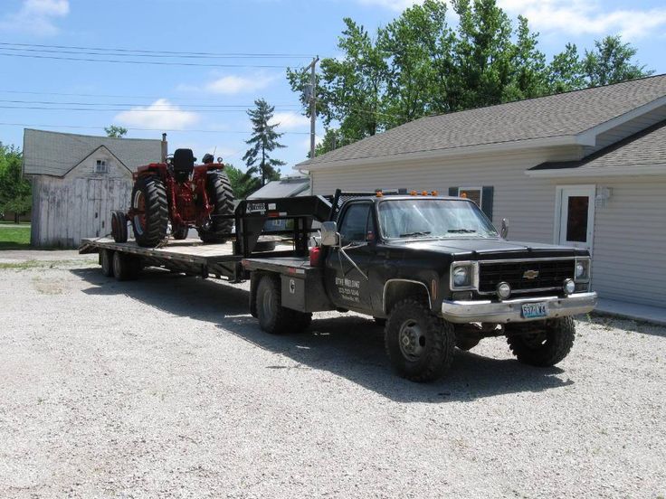 a flatbed tow truck with two large tractors on it's bed parked in front of a house