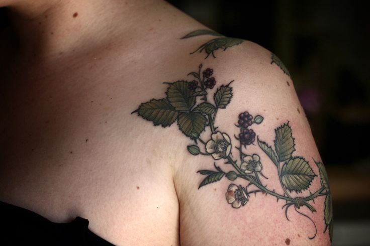 a close up of a person's shoulder with flowers and leaves tattooed on it