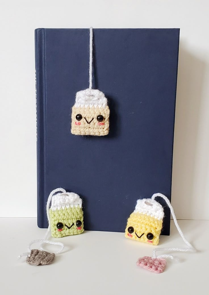 two small crocheted items are hanging on a book with twine strings attached to them