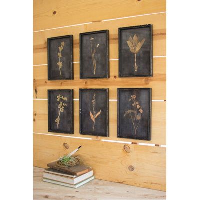 four framed flowers on a wood paneled wall next to a book and planter