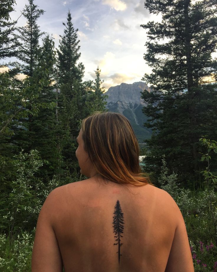 a person with a tattoo on their back standing in front of some trees and flowers