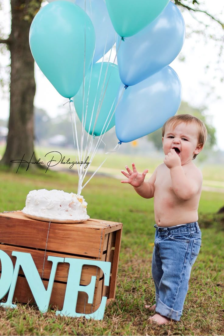 a baby standing next to a wooden crate with balloons