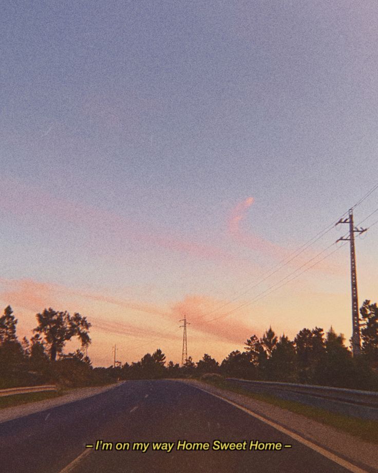 the sun is setting on an empty road with power lines in the distance and trees to the side