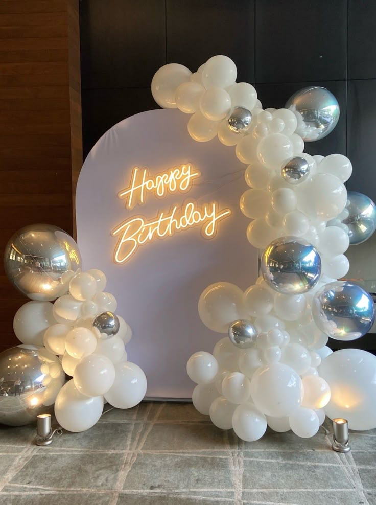 balloon arch with happy birthday written on it and silver balloons around the arch in front