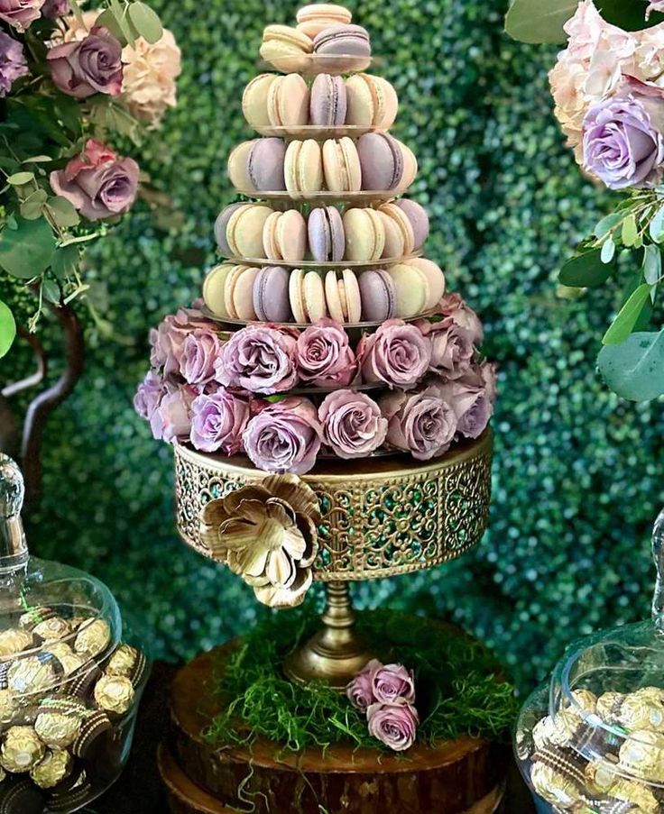 a tower of macaroons and other sweets on a table with flowers in the background