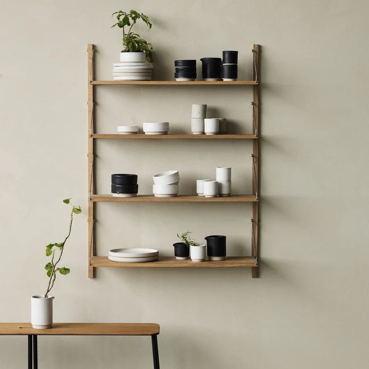 a wooden shelf filled with white dishes and plants next to a wall mounted planter