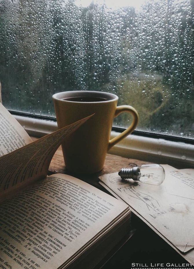 an open book and cup of coffee on a window sill with raindrops