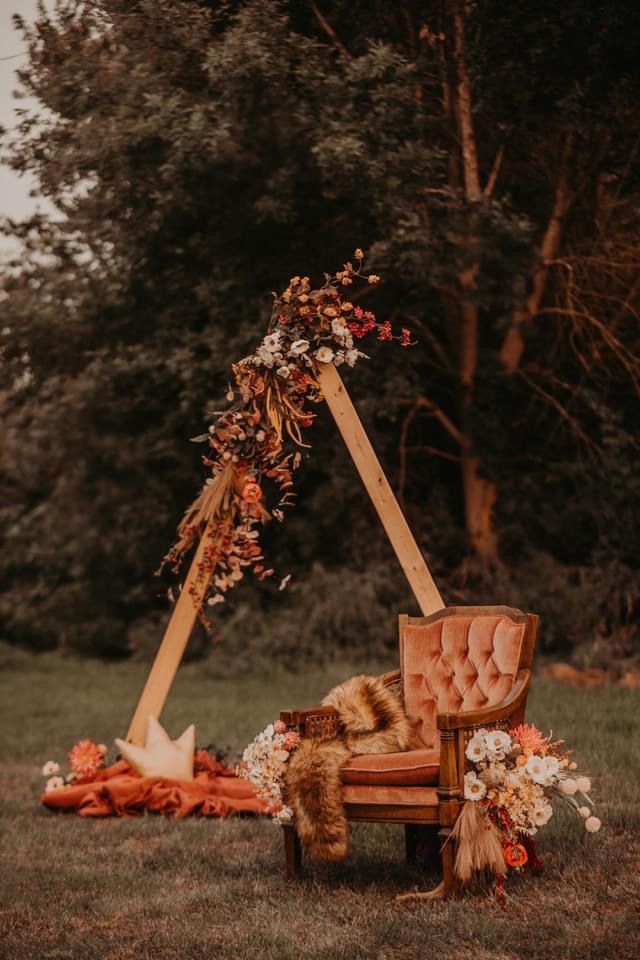 an old chair is set up with flowers and greenery on the back for a wedding ceremony