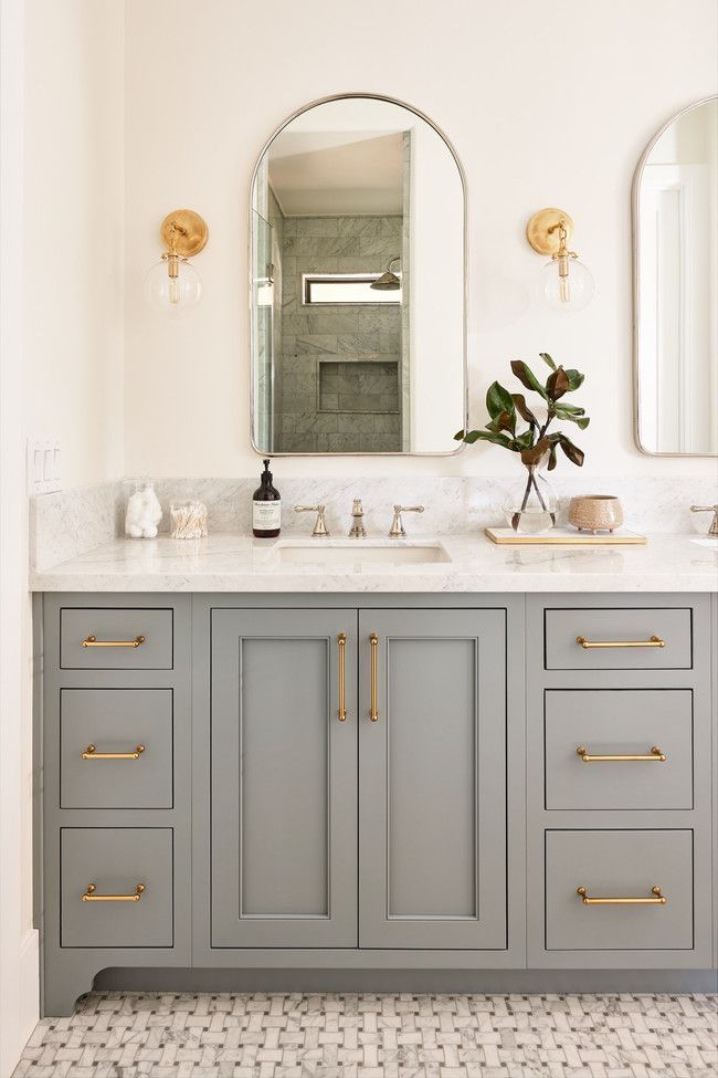 a bathroom vanity with two sinks, mirrors and lights on the wall above it is decorated in white and gold