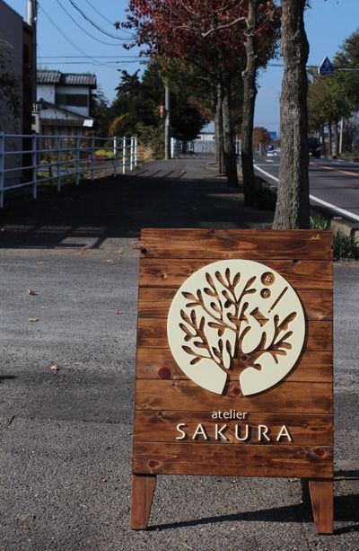 a wooden sign sitting on the side of a road next to a street with trees