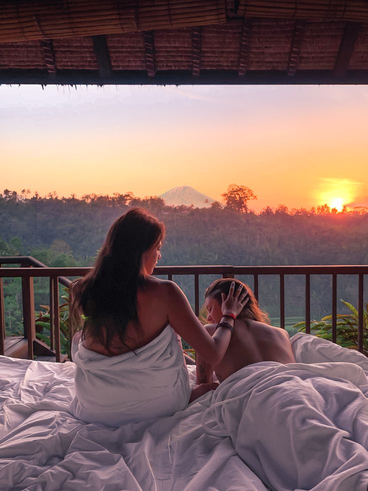 two women sitting on a bed looking at the sunset