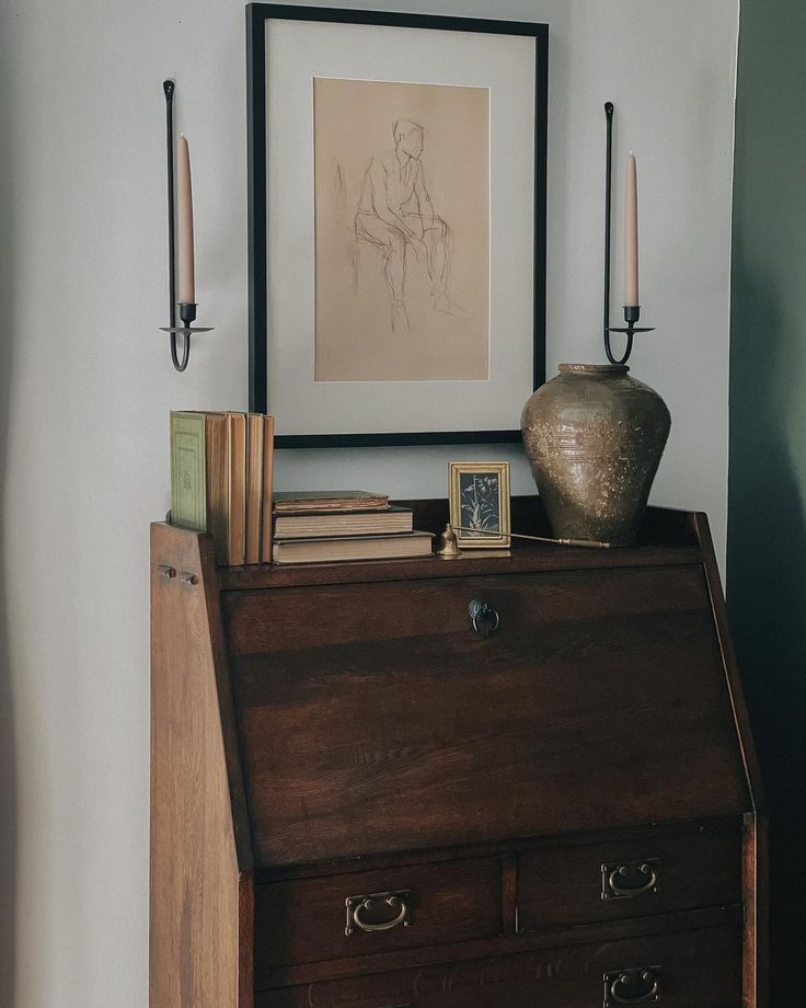 an antique chest with books and candles on it in front of a framed art piece