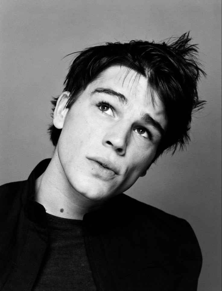 a black and white photo of a young man with his hair in the air, looking at the camera