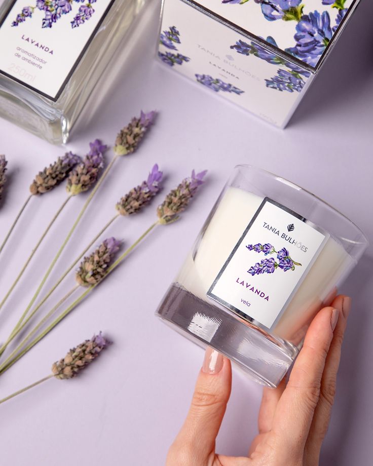 a person holding a candle in front of some lavenders on a purple table with two boxes