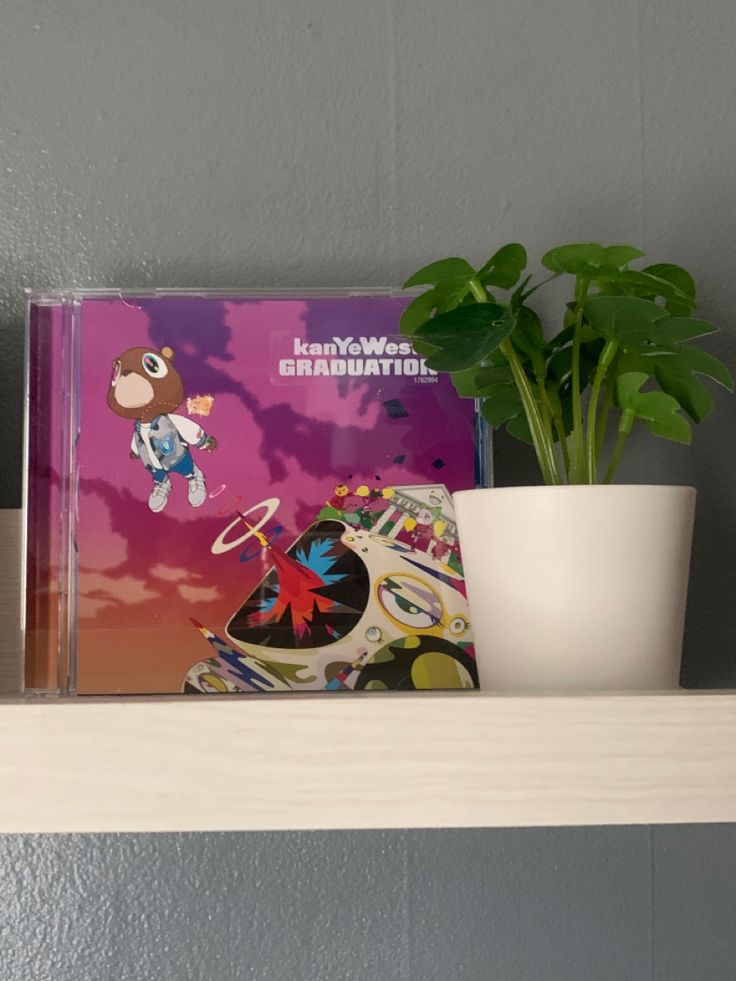 a potted plant sitting on top of a white shelf next to a cd case