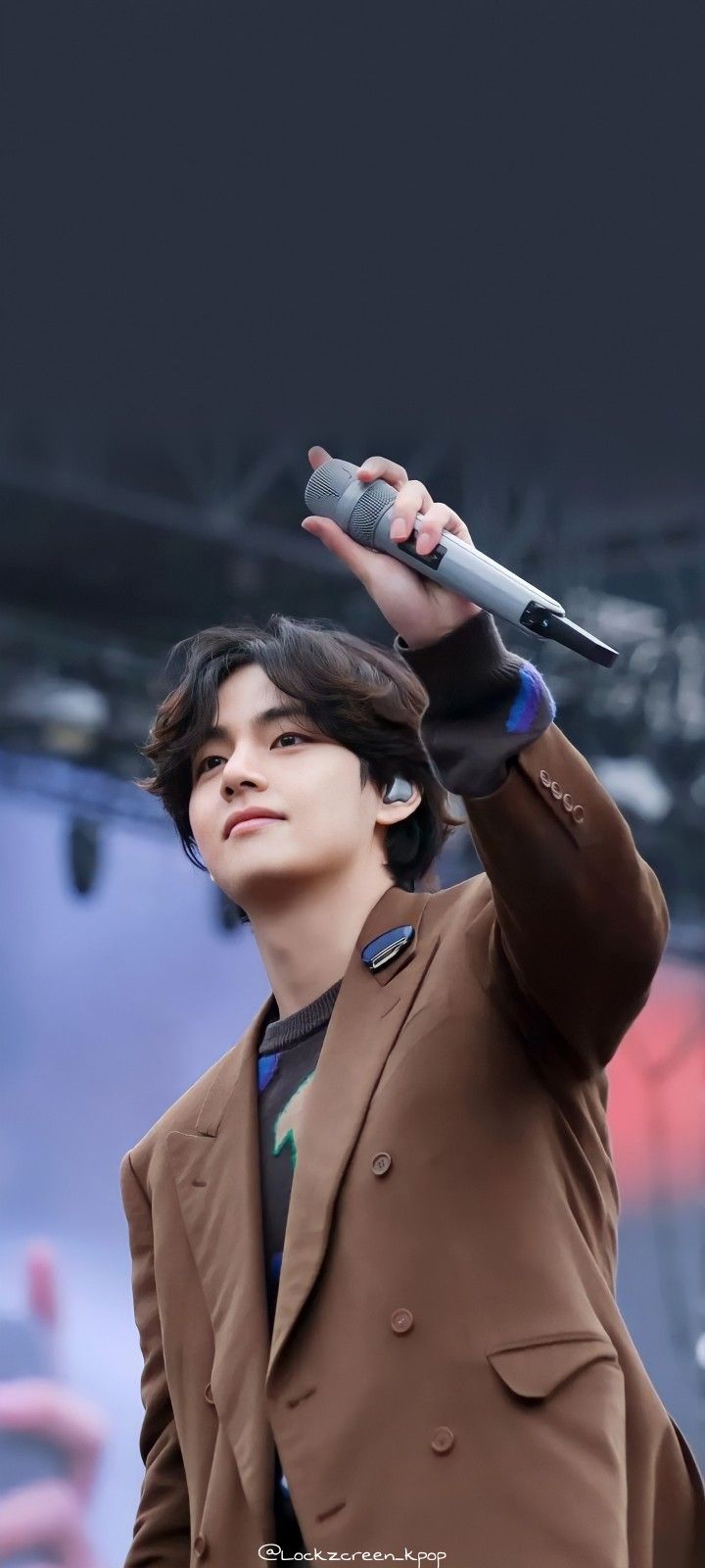 a young man holding a microphone up to his ear while wearing a brown suit and tie