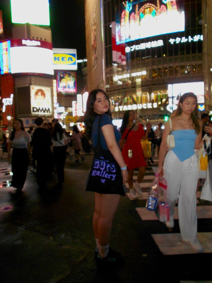 two women walking across a cross walk in the middle of a busy city at night