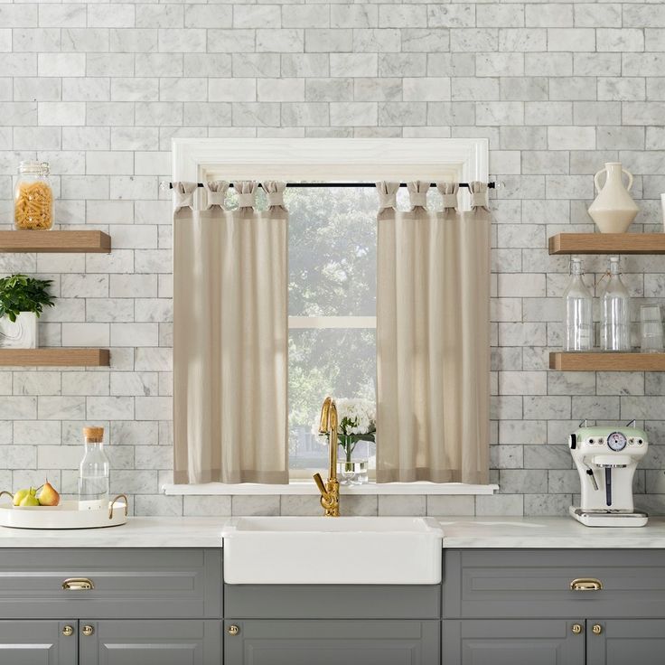 a kitchen with gray cabinets and white brick walls, along with open shelving above the sink