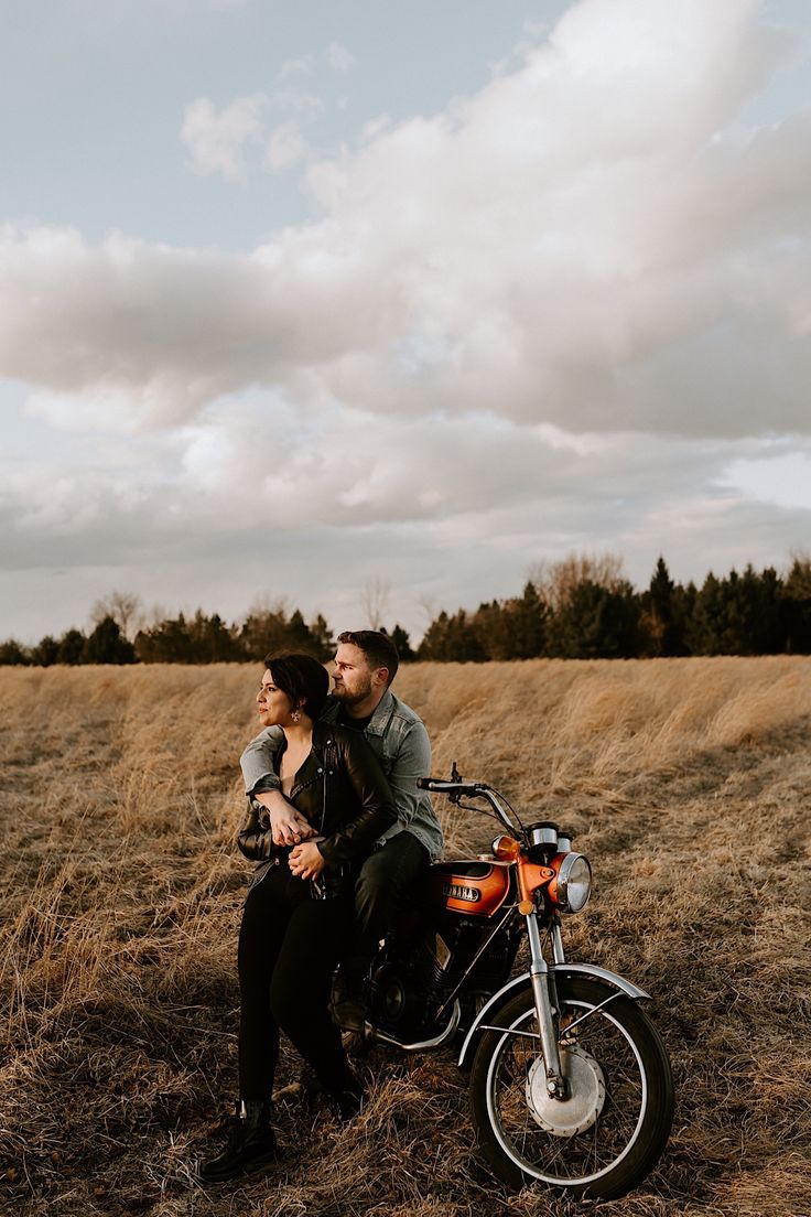 a man and woman are sitting on a motorcycle in the middle of an open field