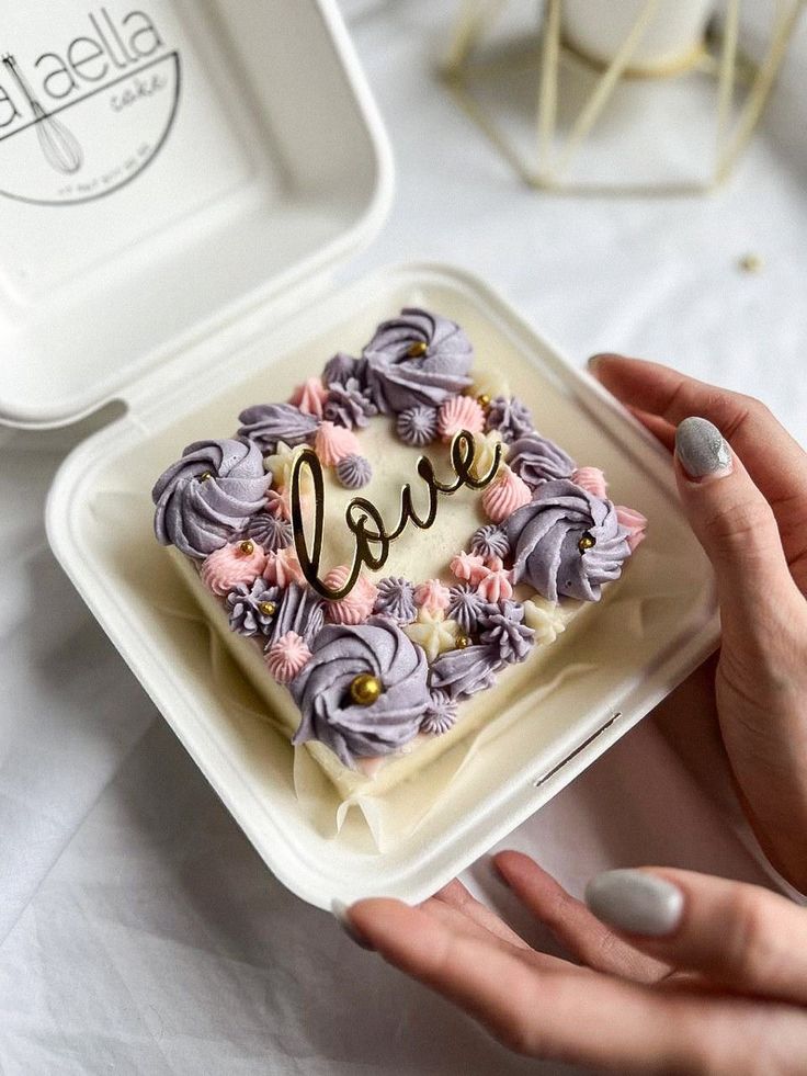 a person holding a cake in their hand with the word love spelled on it and flowers