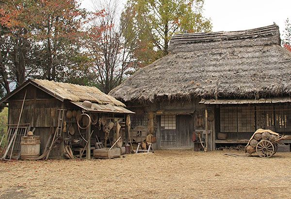 an old farm house with a thatched roof and two wooden wagons in front of it