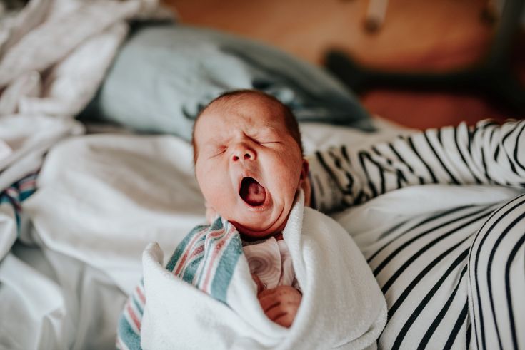 a baby is yawning while wrapped in a blanket