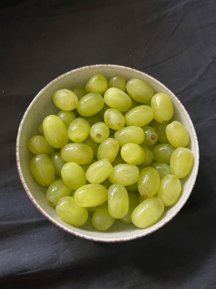 a white bowl filled with green grapes on top of a black cloth covered tablecloth