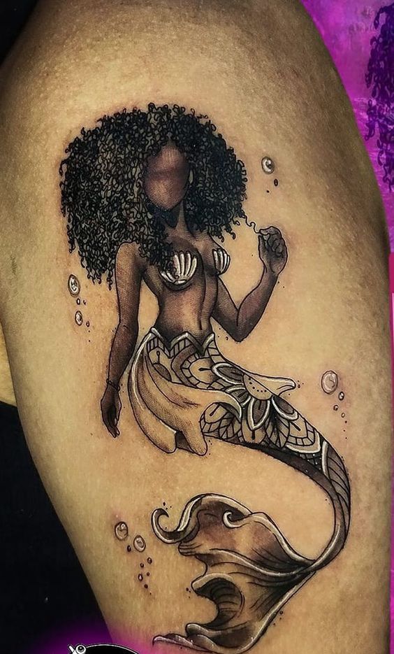 a woman with an afro is sitting on her stomach and has a mermaid tattoo on it