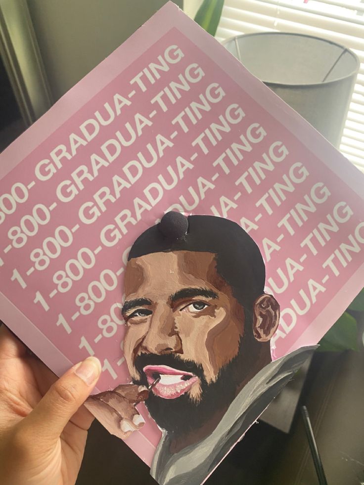 a hand holding up a pink graduation card with the image of a man's face on it