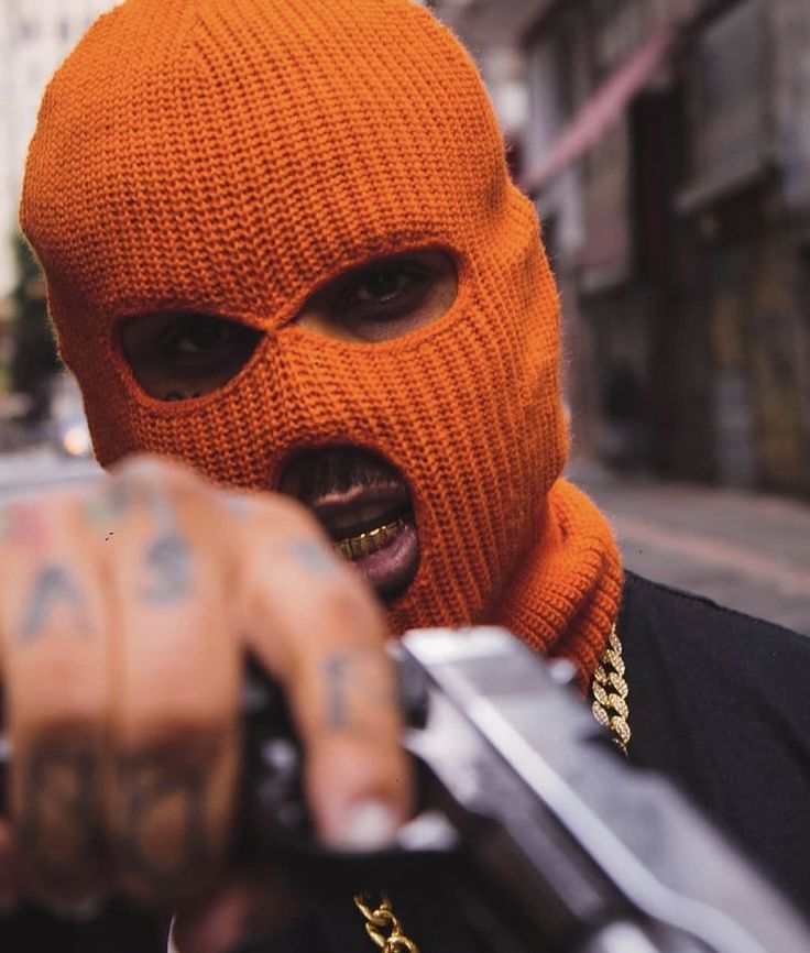 a man in an orange knitted mask holding a knife and pointing at the camera