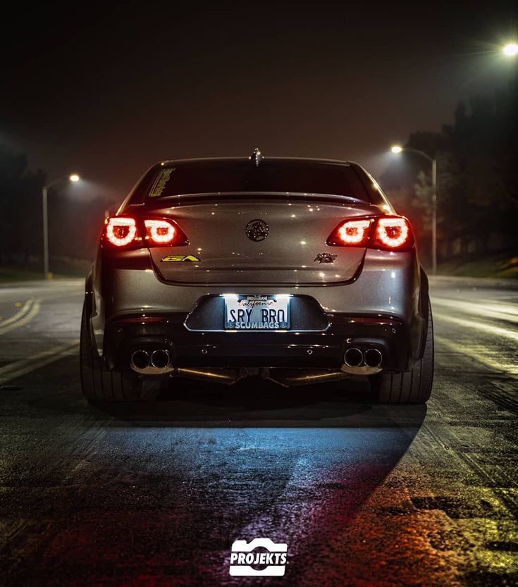 the rear end of a silver car on a road at night with street lights in the background