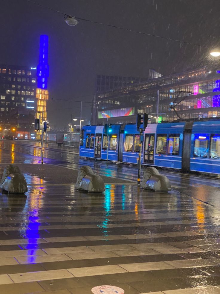 a blue and white train traveling down tracks next to tall buildings in the city at night