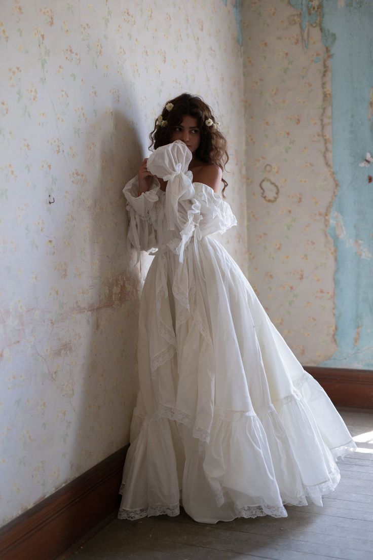 a woman in a white dress leaning against a wall