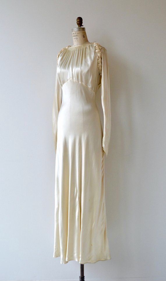 a white dress on a mannequin stand in front of a wall with a light colored background