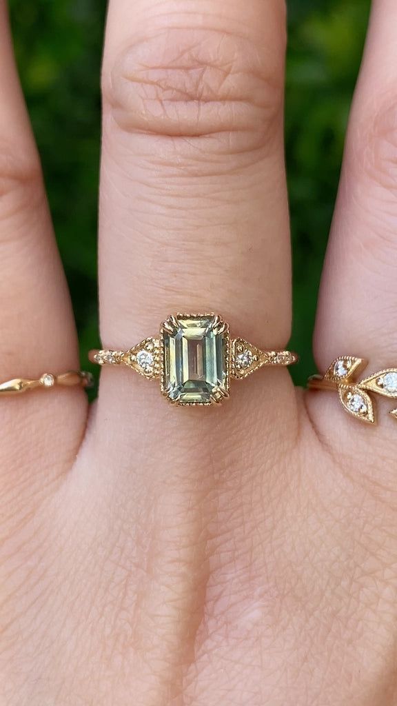 a woman's hand with two rings on it and an emerald stone in the middle