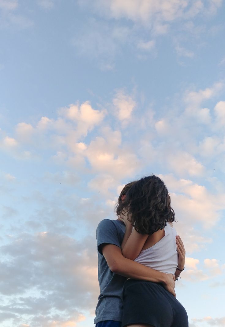 two people embracing each other in front of a cloudy sky